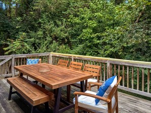 Een houten terras met een tafel en stoelen, omgeven door weelderige begroeiing.