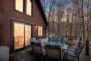 A wooden deck with outdoor furniture, a sliding glass door, and a view of a forest.