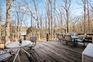 A wooden deck with a round table and chairs, surrounded by trees.