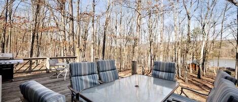 An outdoor deck with a table and striped cushioned seating, surrounded by trees.