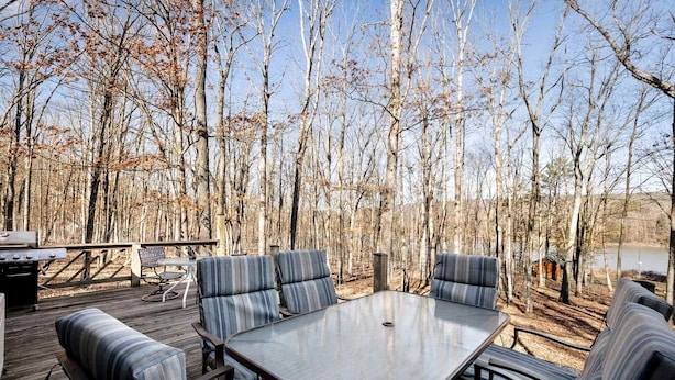 An outdoor deck with a table and striped cushioned seating, surrounded by trees. - Lustrous Lakefront Cabin Oasis near Lake Ferndale in West Virginia (Springfield)