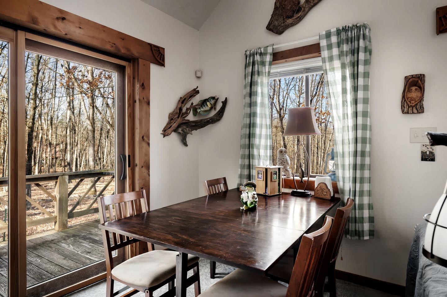 Zona pranzo con tavolo in legno, sedie e vista su alberi dalla finestra.