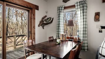 Zona pranzo con tavolo in legno, sedie e vista su alberi dalla finestra.