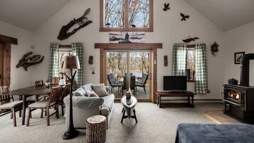 A cozy living room with a fireplace, a dining area, and a large window overlooking a natural landscape.