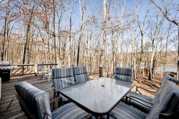 An outdoor deck with a table and striped cushioned seating, surrounded by trees.