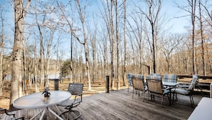 A wooden deck with a round table and chairs, surrounded by trees. - Lustrous Lakefront Cabin Oasis near Lake Ferndale in West Virginia (Springfield)
