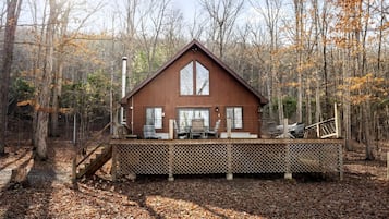 A cabin with a deck, surrounded by trees and a forest.