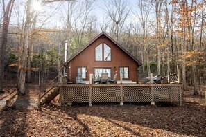 A cabin with a deck, surrounded by trees and a forest.