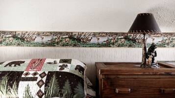 A bedroom with a bed, a wooden dresser, a lamp, and a wildlife-themed tapestry on the wall.