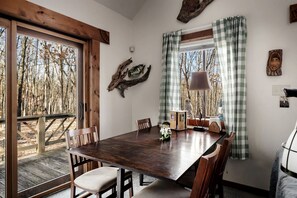 A dining area with a wooden table, chairs, and a view of trees through the window.