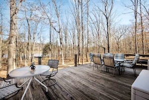 A wooden deck with a round table and chairs, surrounded by trees.