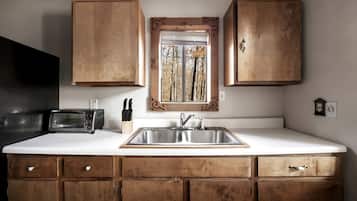 A kitchen with wooden cabinets, a stainless steel sink, a window with a view of trees, and a toaster.