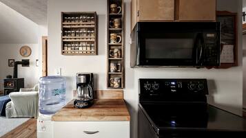 A kitchen with a water dispenser, coffee maker, microwave, and stove.