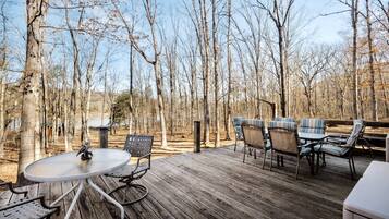 A wooden deck with a round table and chairs, surrounded by trees.