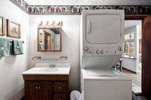 Un baño pequeño con un lavamanos blanco, tocador de madera, un espejo con iluminación y una lavadora blanca.