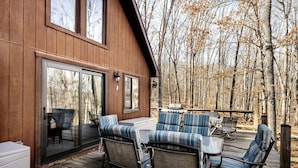 A wooden deck with outdoor seating and a sliding glass door leading to a covered patio area. - Lustrous Lakefront Cabin Oasis near Lake Ferndale in West Virginia (Springfield)