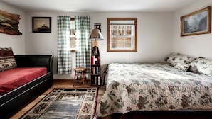 A cozy bedroom with a bed, a chair, a small table, a bookshelf, and a window with curtains. - Lustrous Lakefront Cabin Oasis near Lake Ferndale in West Virginia (Springfield)