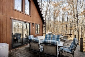 Eine Holzterrasse mit Sitzgelegenheiten im Freien und einer Glastür, die zu einer überdachten Patio führt.