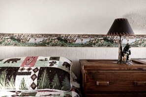A bedroom with a bed, a wooden dresser, a lamp, and a wildlife-themed tapestry on the wall.