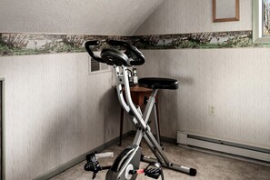 A stationary bike in a corner of a room with a textured wall and a window.