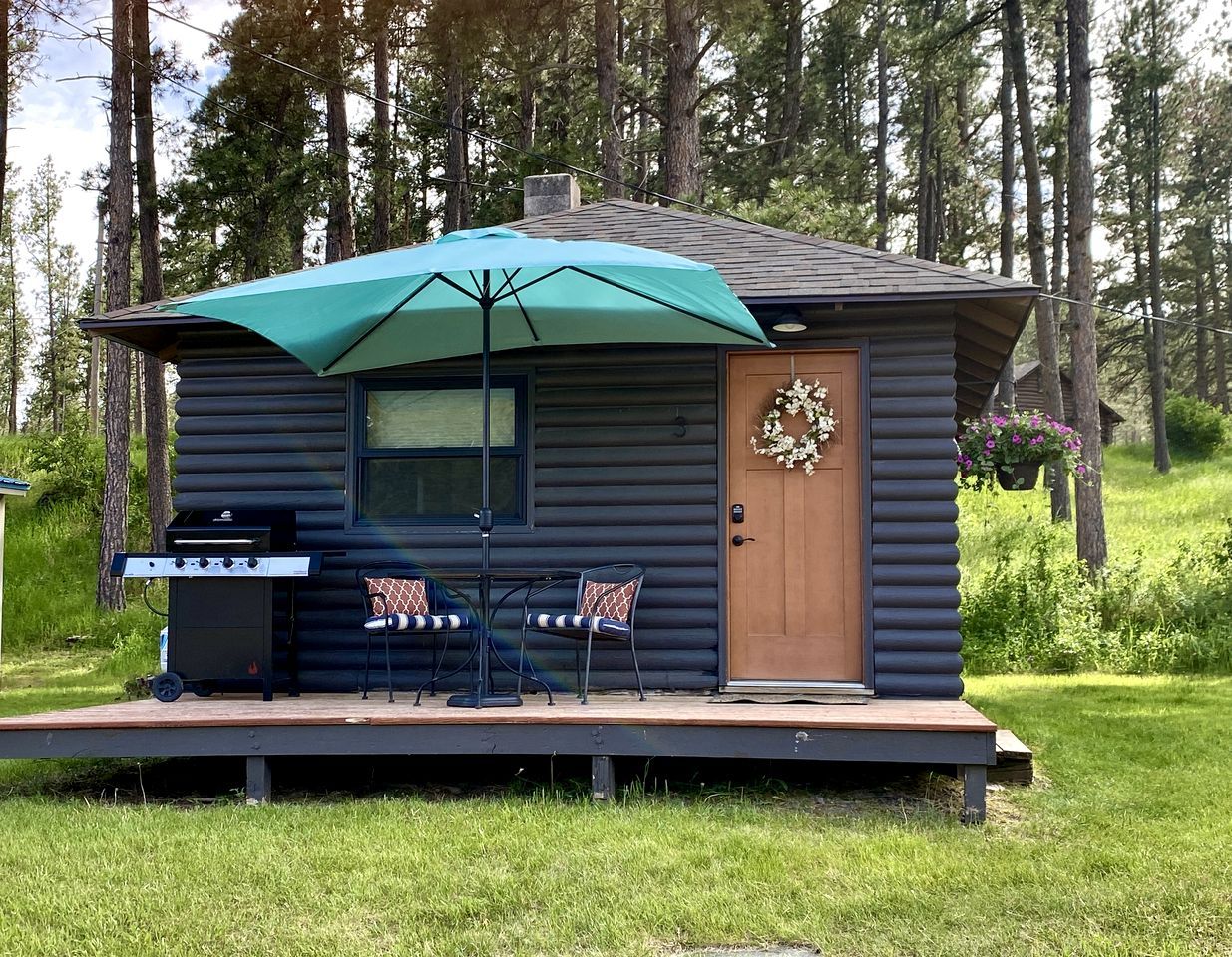Eine Blockhütte mit Veranda, Grill und Gartenmöbeln.