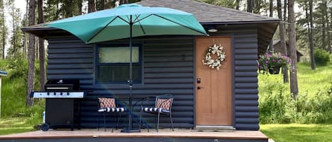 A log cabin with a porch, a grill, and outdoor seating.