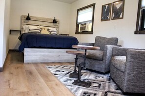 A bedroom with a bed, a chair, a small table, a rug, and a window.