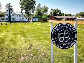 A sign for The Legacy Inn in Luray, VA, with a well-maintained lawn and a large white building in the background.