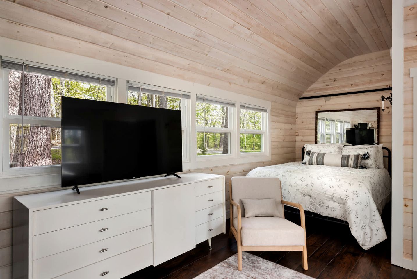 A bedroom with a TV, a bed, a chair, and a dresser.
