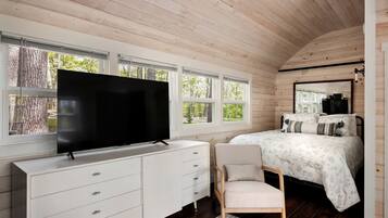 A bedroom with a TV, a bed, a chair, and a dresser.