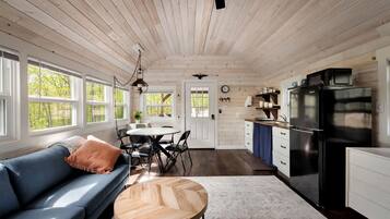 L’intérieur d’une cabane comprend un coin repas, une cuisine et un canapé bleu, ainsi qu’une table en bois.
