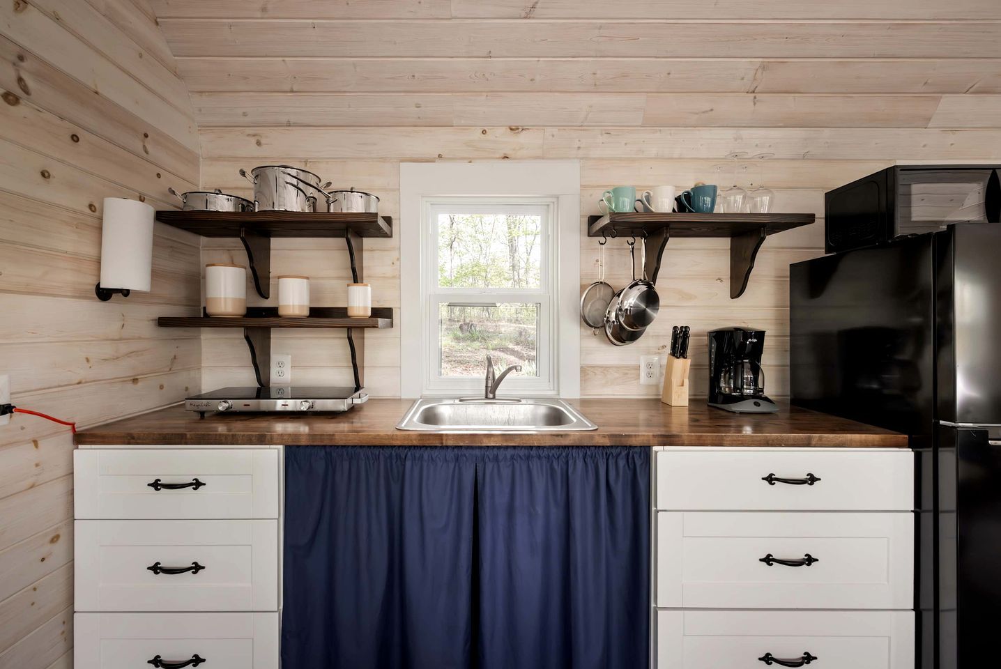 A kitchen with wooden walls, a sink, cabinets, and a window.