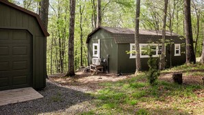 A small wooden cabin with a garage, surrounded by a forest. - Modern Tiny Cabin with Game Room & Fire Pit in West Virginia (Great Cacapon)