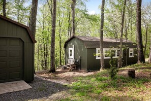 A small wooden cabin with a garage, surrounded by a forest.