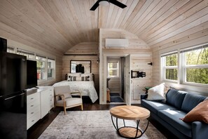 A cabin interior with a bed, sofa, TV, and kitchenette.