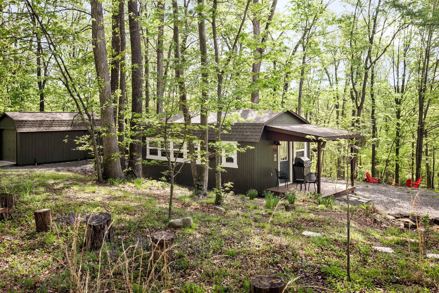 A cabin with a porch, a grill, and red chairs.