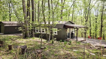 A cabin with a porch, a grill, and red chairs.