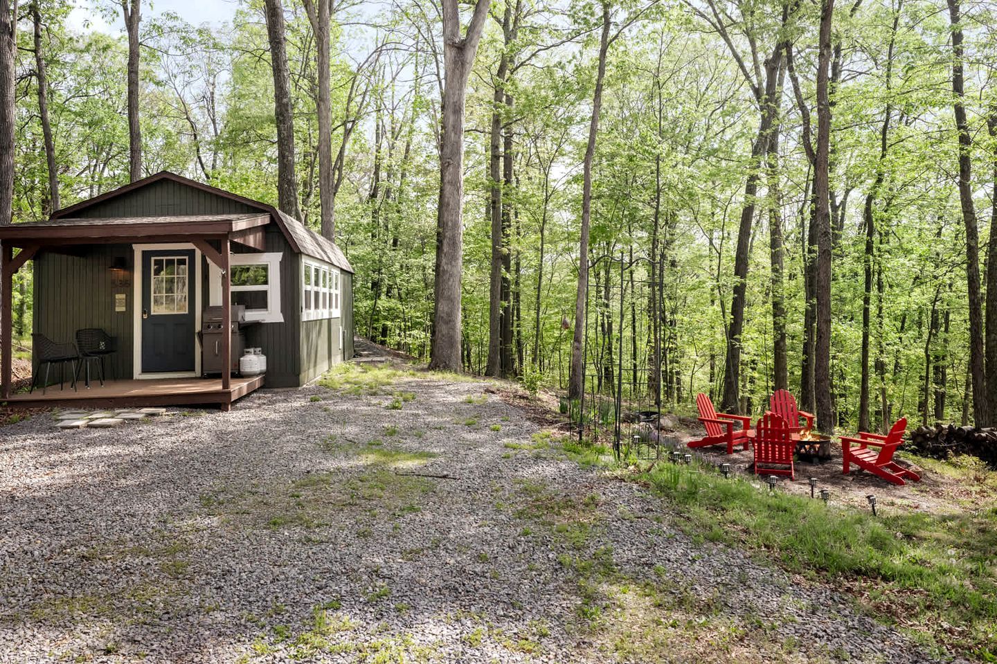 A cabin with a porch, a grill, and red Adirondack chairs.