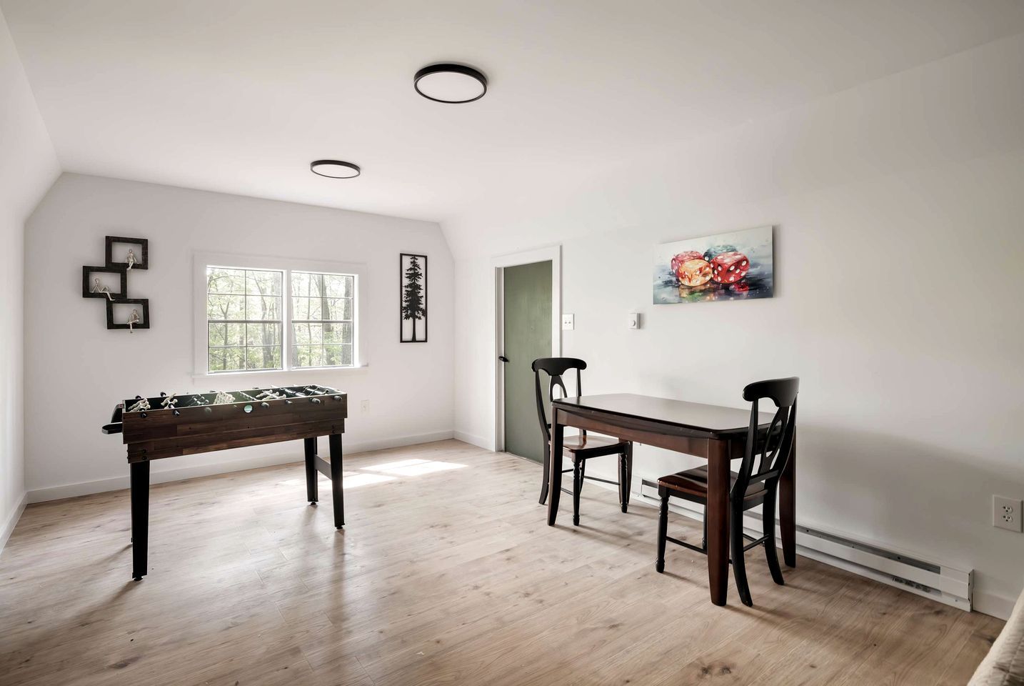 A room with a foosball table, a dining table with chairs, a window, and a door.