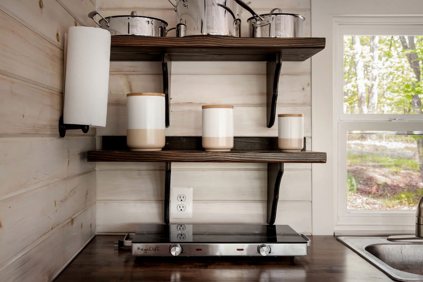A kitchen with wooden shelves, a Megaflex induction cooktop, and a window with a view of trees.