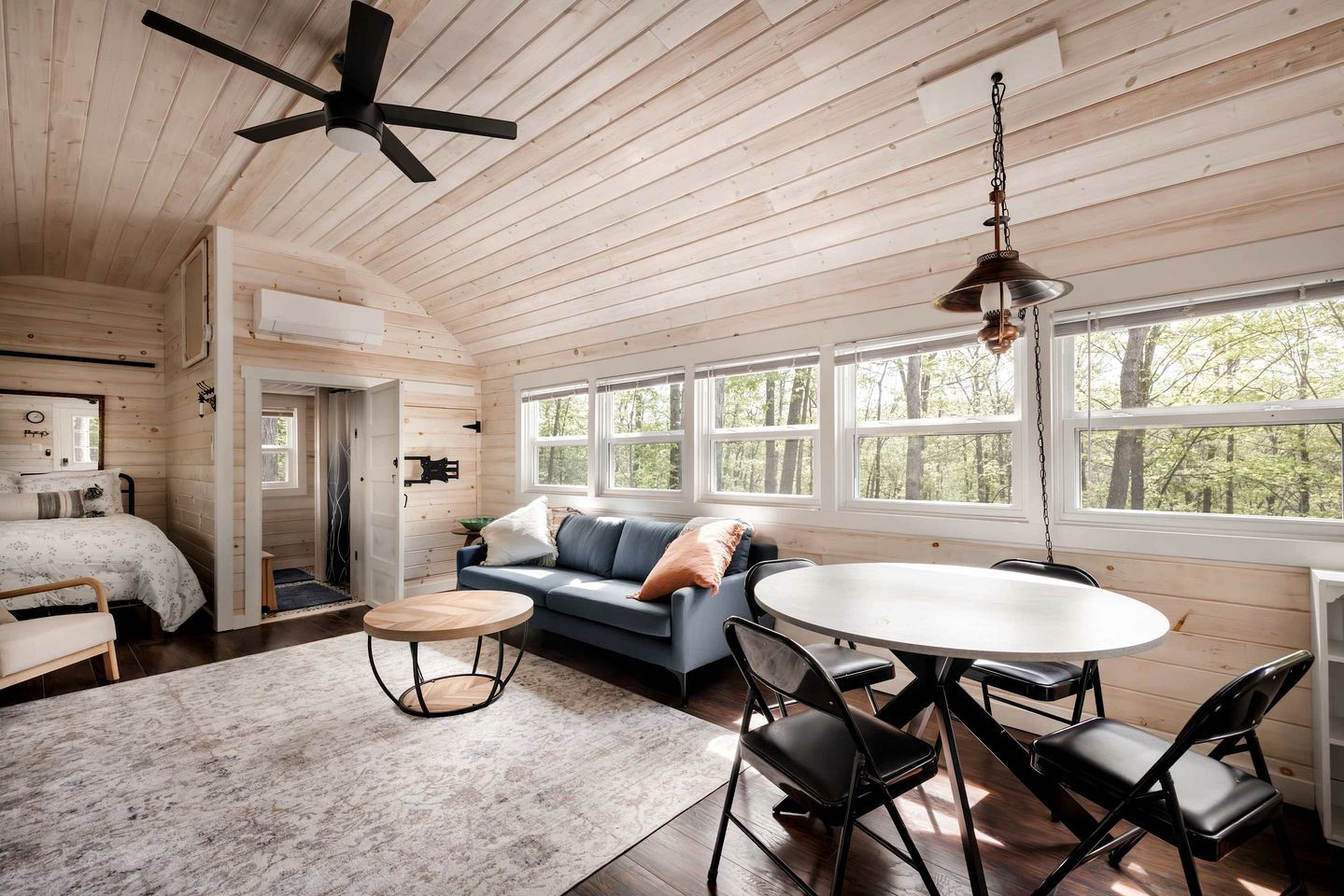 A cabin interior with a bed, sofa, dining table, chairs, and a ceiling fan.