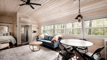 A cabin interior with a bed, sofa, dining table, chairs, and a ceiling fan.