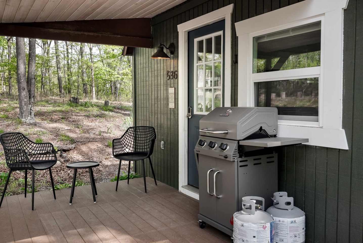A covered outdoor area with a grill, two chairs, and propane tanks.