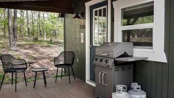 A covered outdoor area with a grill, two chairs, and propane tanks.