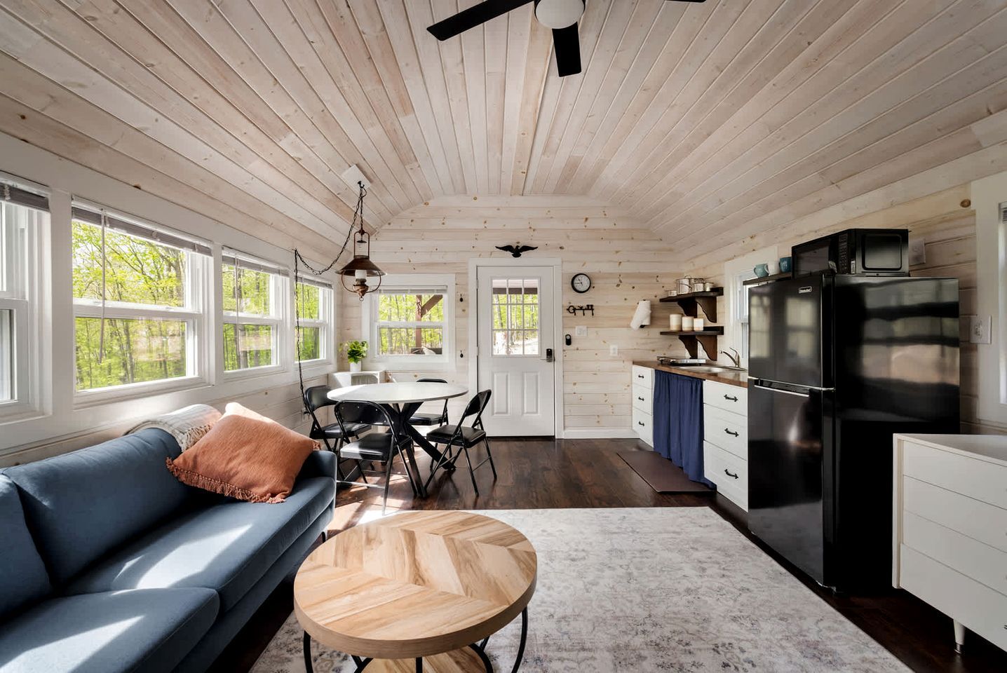A cabin interior with a dining area, kitchen, and a blue sofa with a wooden table.