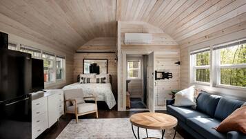A cabin interior with a bed, sofa, TV, and kitchenette.