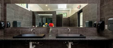 A modern bathroom with two sinks, dark tiles, a large mirror, and a terrazzo floor.