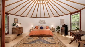 A bedroom with a large bed, a wooden ceiling, a dining table, and a small kitchen area. - Creekside Yurt - The Dreamer (Balsam Grove)