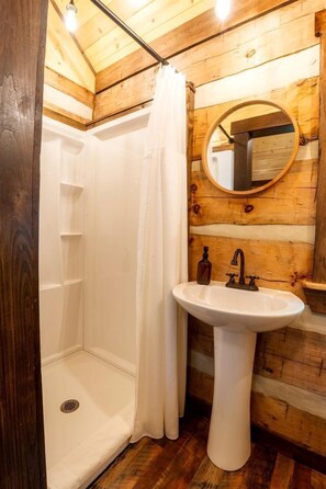 A wooden cabin bathroom with a shower, a sink, and a mirror.
