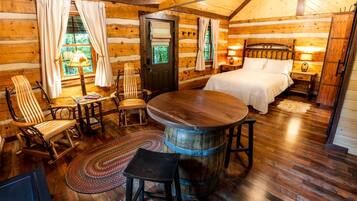 Une chambre aménagée dans un chalet en rondins, avec un lit, une table en bois, une chaise, un petit tapis et un tonneau en bois.